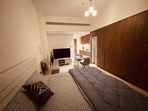 A compact living space with a sofa, a TV, a small dining table, and a kitchenette.