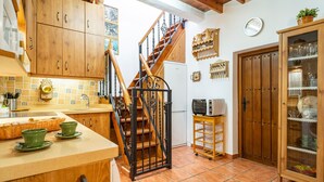 Eine Küche mit Holzschränken, einer gefliesten Spritzschutzwand, einer Holztreppe, einem Kühlschrank, einer Mikrowelle und einem Glaskasten mit Geschirr.