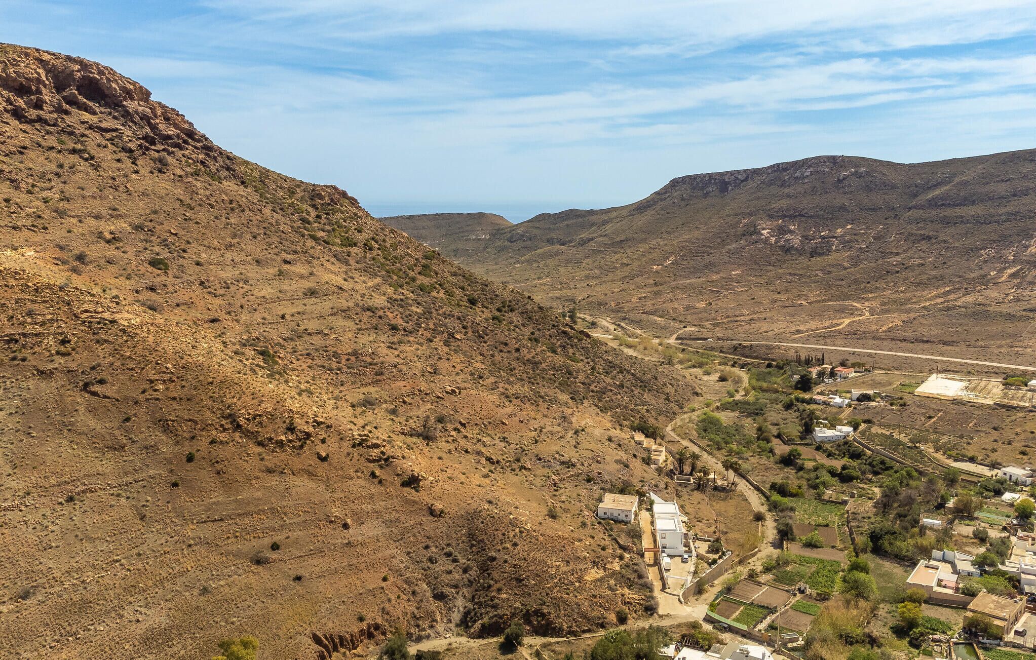 A rural landscape with a valley, a small settlement with houses, and a distant mountain range.