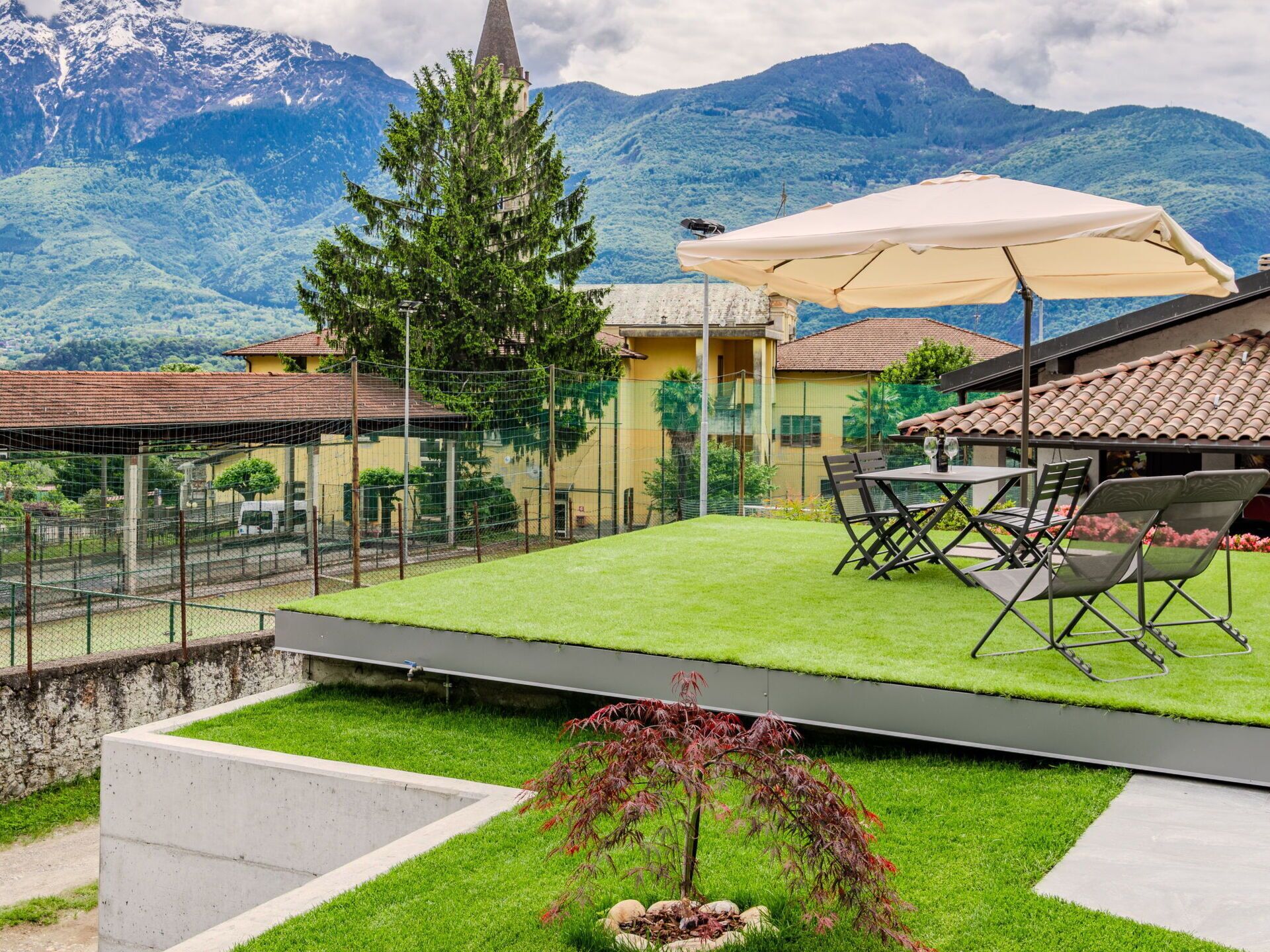 Un patio con una mesa y sillas, un árbol pequeño y vistas de montañas.