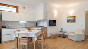 A modern kitchen with white cabinets, a dining table with chairs, a TV mounted on the wall, and a painting on the wall. - Nice apartment for 4 people with WIFI, terrace and pets allowed (Domaso)