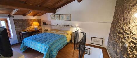 A bedroom with a bed, a desk, a lamp, and a stone wall.