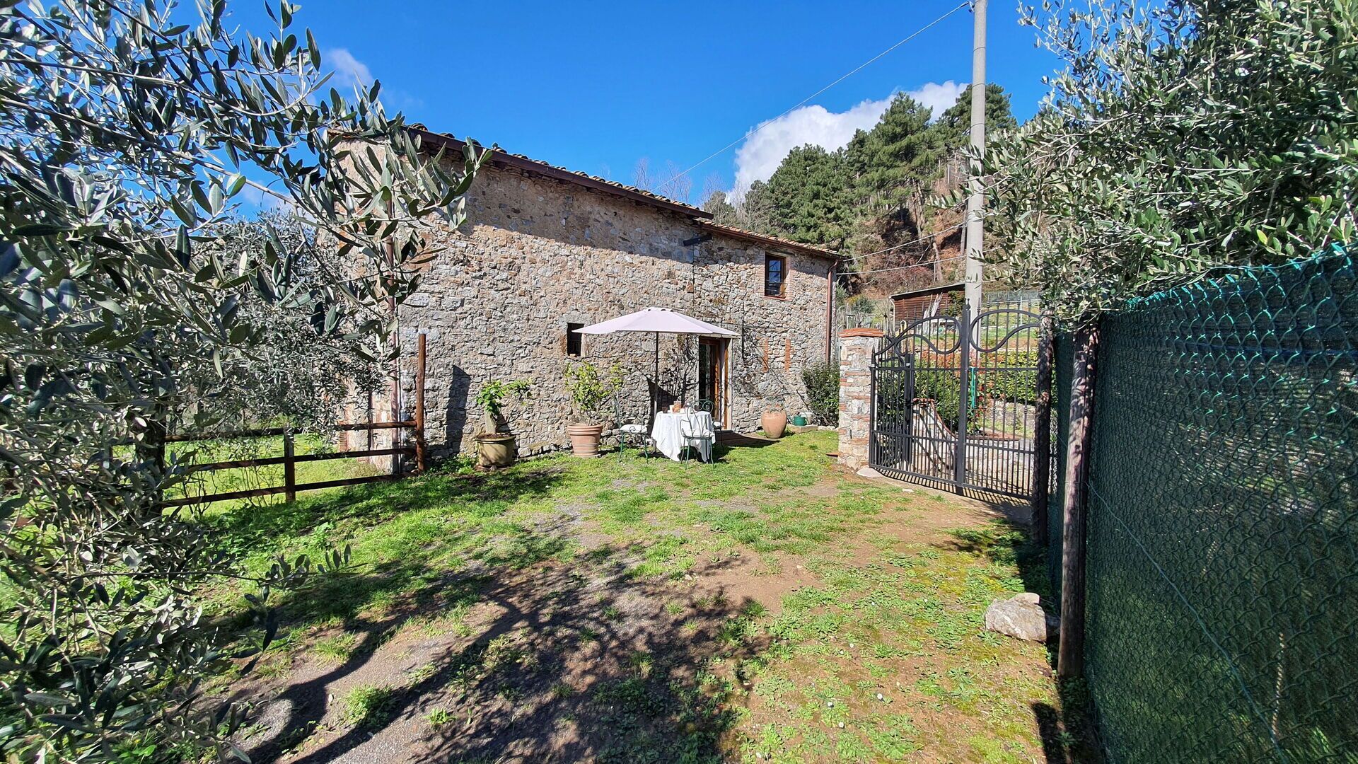 A stone building with a rustic exterior, a fenced yard, and a table with chairs under an umbrella.