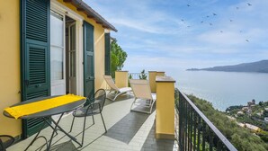 En balkon med et bord og stole, med udsigt over vand og en fjerntliggende kystlinje.