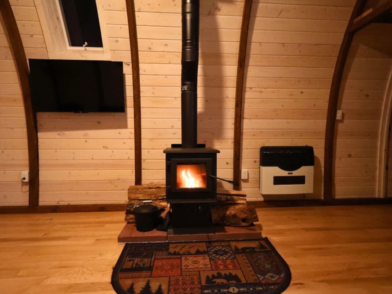 Een kamer met een houtkachel, een raam en een vuilnisbak.