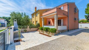 Ein zweistöckiges Haus mit überdachter Veranda, einem gepflasterten Weg und einem kleinen Garten.