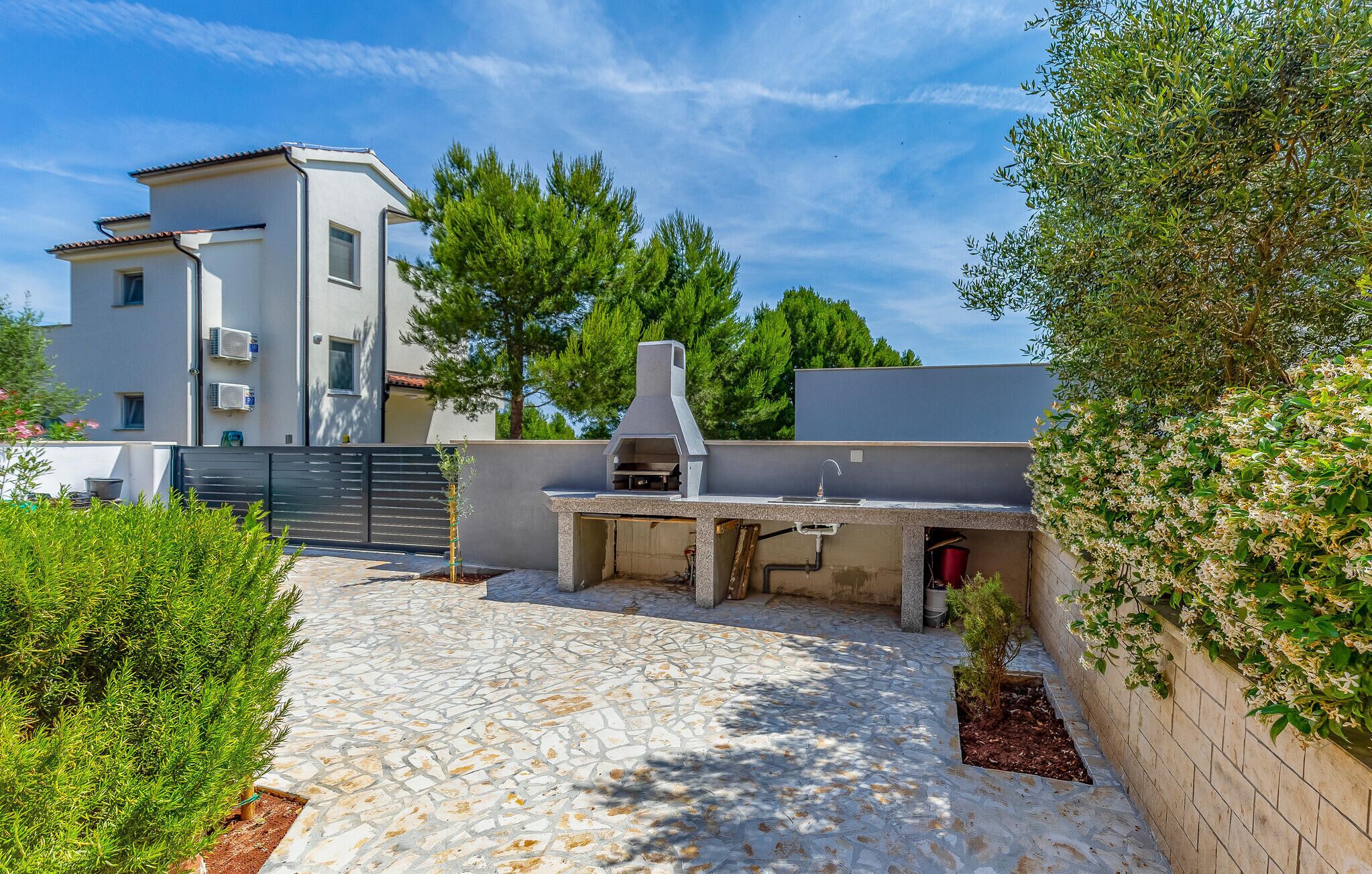 A modern outdoor kitchen with a stone-tiled patio, a built-in grill, and a view of a residential building in the background.