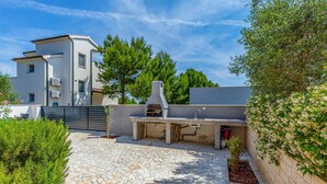 Eine moderne Außenküche mit Steinplatten-Terrasse, integriertem Grill und Blick auf ein Wohngebäude im Hintergrund.