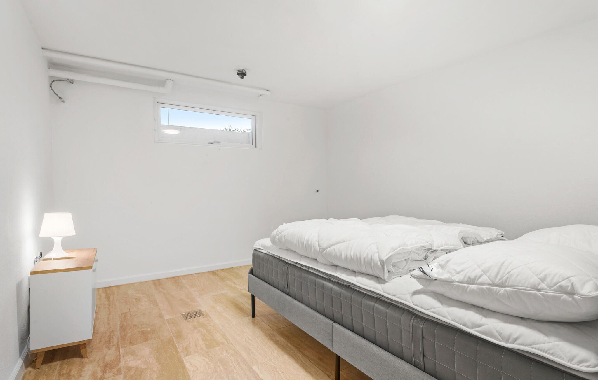 Ein kleines, sauberes Zimmer mit einem Bett, einem Nachttisch und einem Fenster.