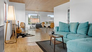 Ein modernes Wohnzimmer mit einem blaugrünen Sofa, Holzböden und einem Essbereich mit Tisch und Stühlen.
