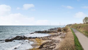 Ein Küstenpfad mit Blick auf das Meer und einer Brücke in der Ferne.