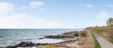 A coastal path with a view of the sea and a bridge in the distance.