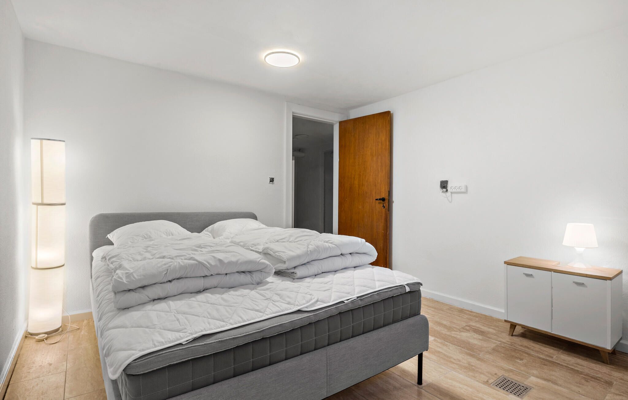 Een slaapkamer met een bed, een bedlampje, een kledingkast en een deur naar een andere kamer.