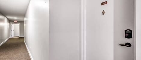 A hallway with a white door, an exit sign, and a doorbell.