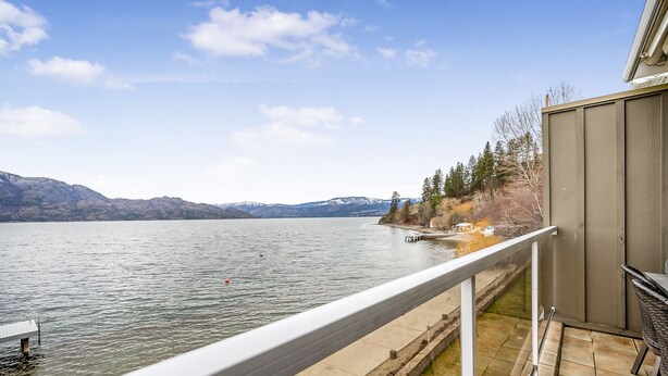 A balcony with a view of a lake, mountains, and a dock with boats. - Spacious Lakefront Condo w Amazing View (West Kelowna)