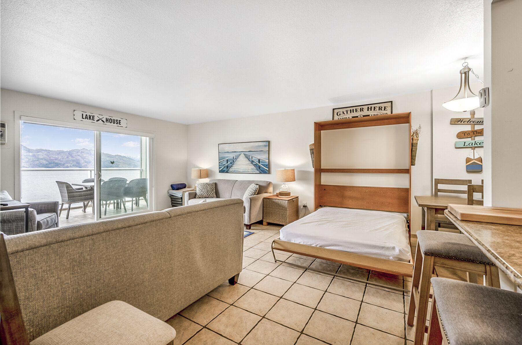 A hotel room with a bed, a sofa, a desk, and a chair. There is a view of a lake through the window.