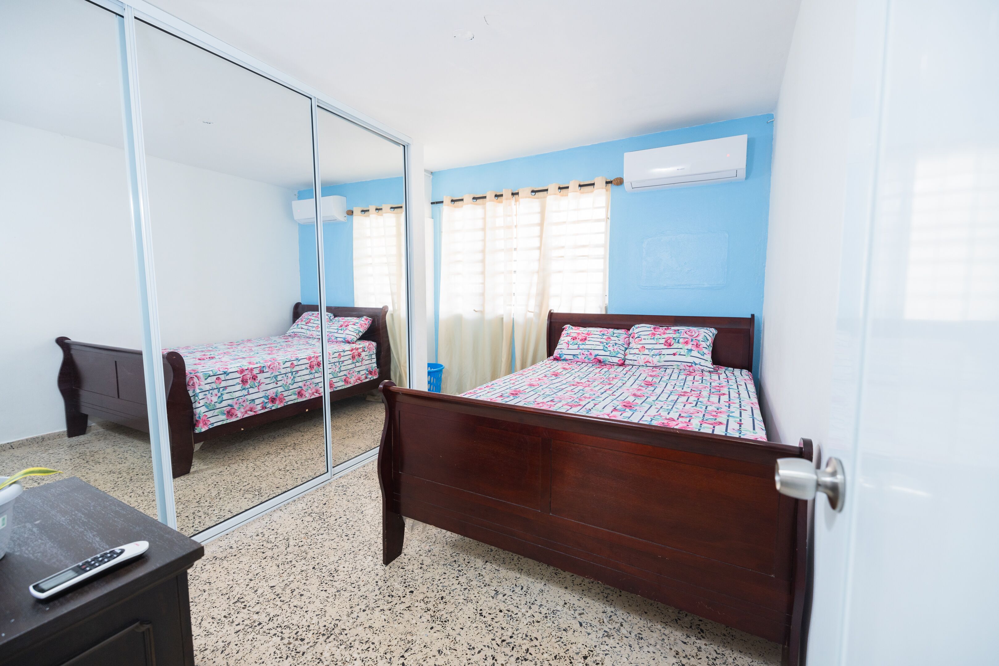 Un dormitorio con dos camas de madera, un espejo, un armario y un equipo de aire acondicionado.