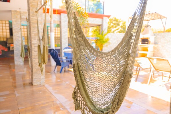 A hammock suspended between pillars in a room with a tiled floor and a view of an outdoor patio area.