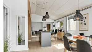 A modern kitchen with a central island, black pendant lights, and a dining area with chairs and a table.