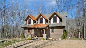 A two-story house with a stone foundation, a front porch, and a gravel driveway.