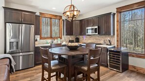 A modern kitchen with dark wood cabinets, stainless steel appliances, and a large dining table surrounded by chairs.