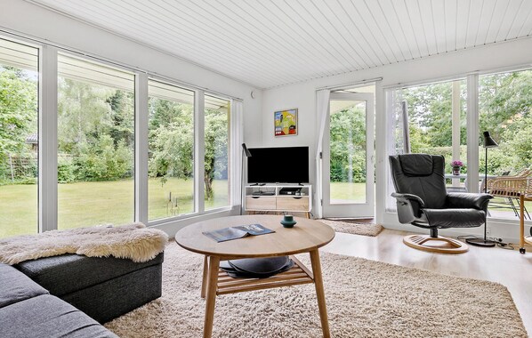 Una sala de estar moderna con un televisor grande, asientos cómodos y vistas a un exuberante jardín.