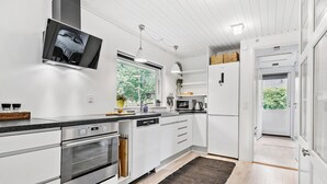 Een moderne keuken met witte kasten, een ingebouwde oven, een magnetron en een koffiezetapparaat. Er is een raam dat natuurlijk licht en uitzicht op groen biedt.