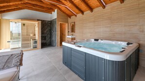 Ruime binnenruimte met een groot bubbelbad, houten balken en een moderne badkamer met een glazen douchecabine.