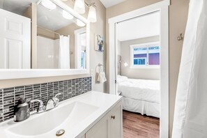 Un baño con lavamanos blanco, espejo y salpicadero de azulejos. Se ve una ventana con vistas a un edificio.