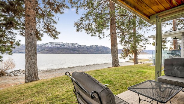Un patio con vistas a un lago y montañas, un espacio de estar cubierto y una mesa.