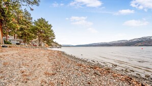 Una propiedad junto al lago con playa de grava, un cobertizo pequeño y un muelle que se adentra en el agua.