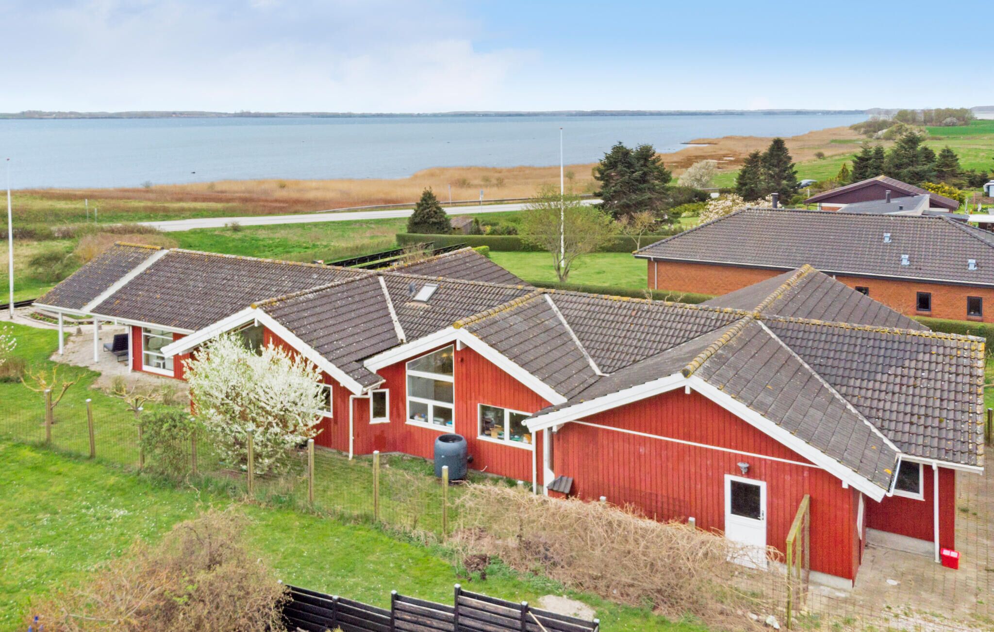 Række røde bygninger med grå tage, sandsynligvis boliger, beliggende nær vand og en vej.