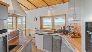 Uma cozinha moderna com bancadas de madeira, armários cinzas e vista para a praia.