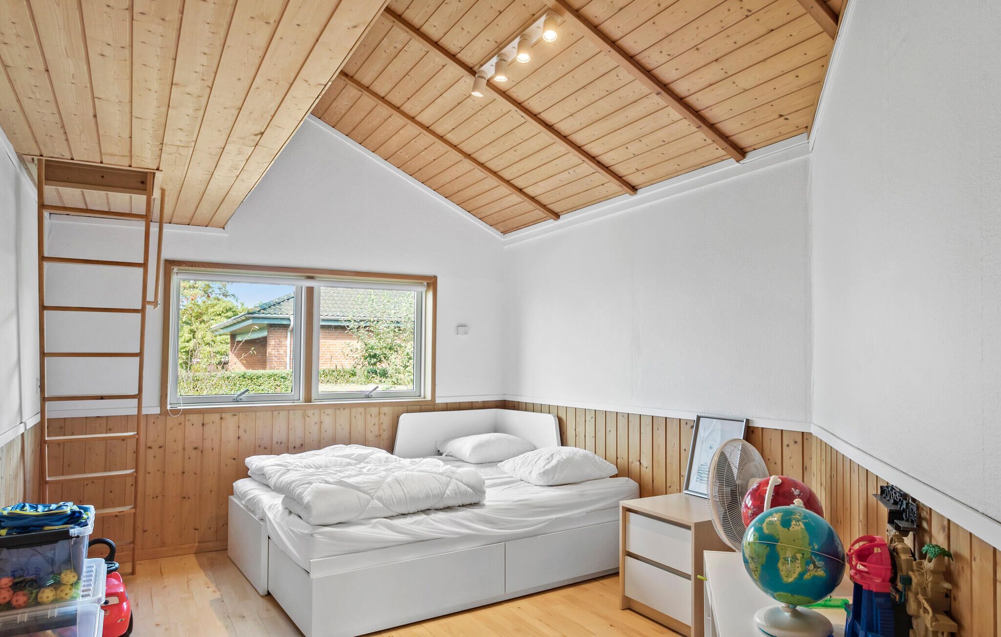 Een slaapkamer met een hoogslaper, houten plafond, een raam met uitzicht, een bureau en een wereldbol.