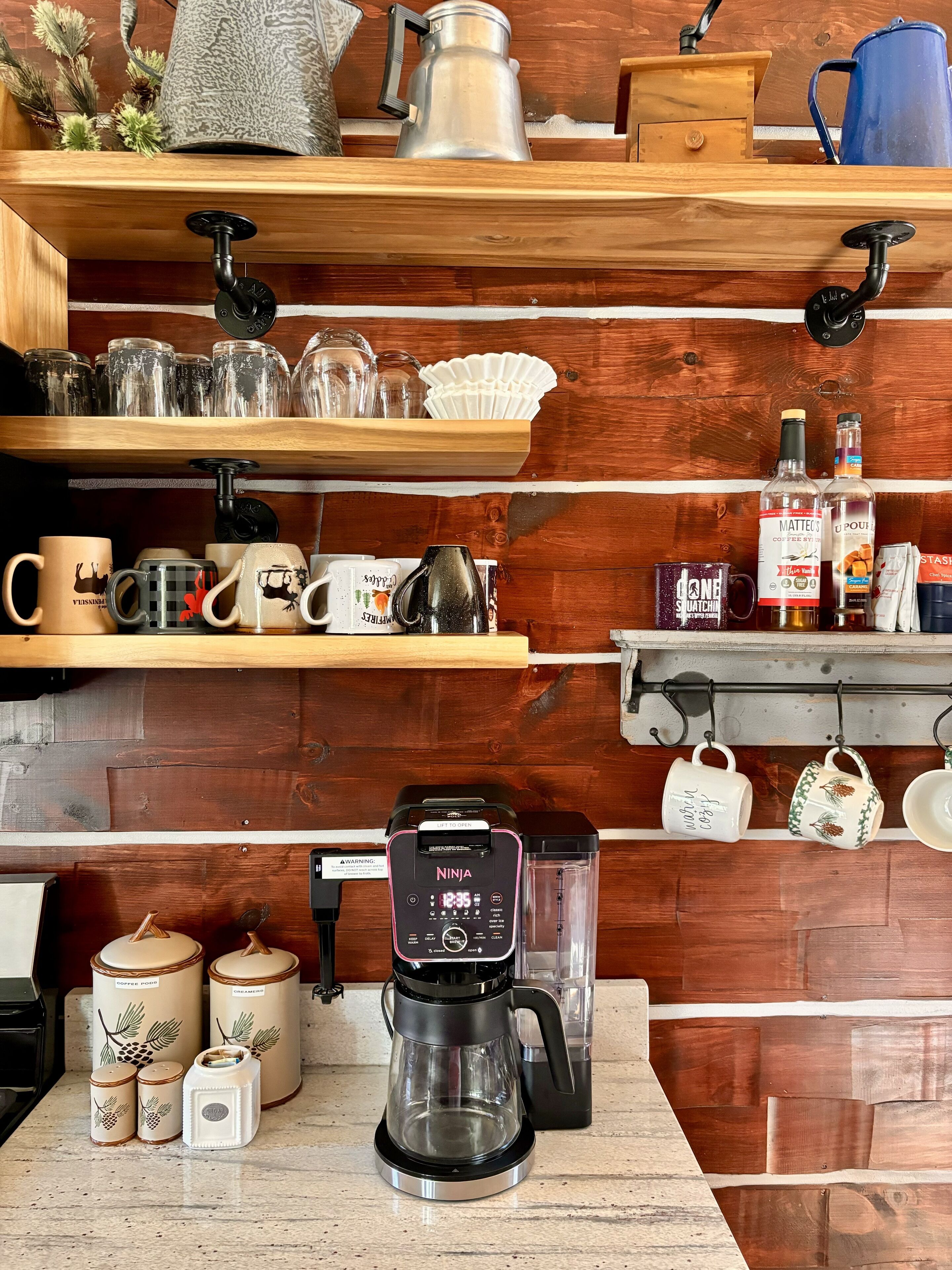 A kitchen with wooden shelves holding glassware, mugs, and a coffee maker.