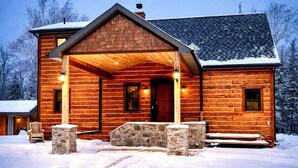 Une cabane en rondins avec un porche en pierre, une cheminée et un paysage enneigé.