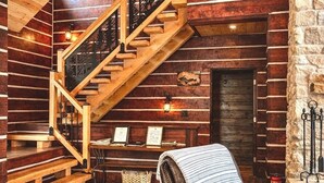 L’intérieur d’une cabane en rondins, avec un escalier en bois, un fauteuil en cuir et un mur en pierre.
