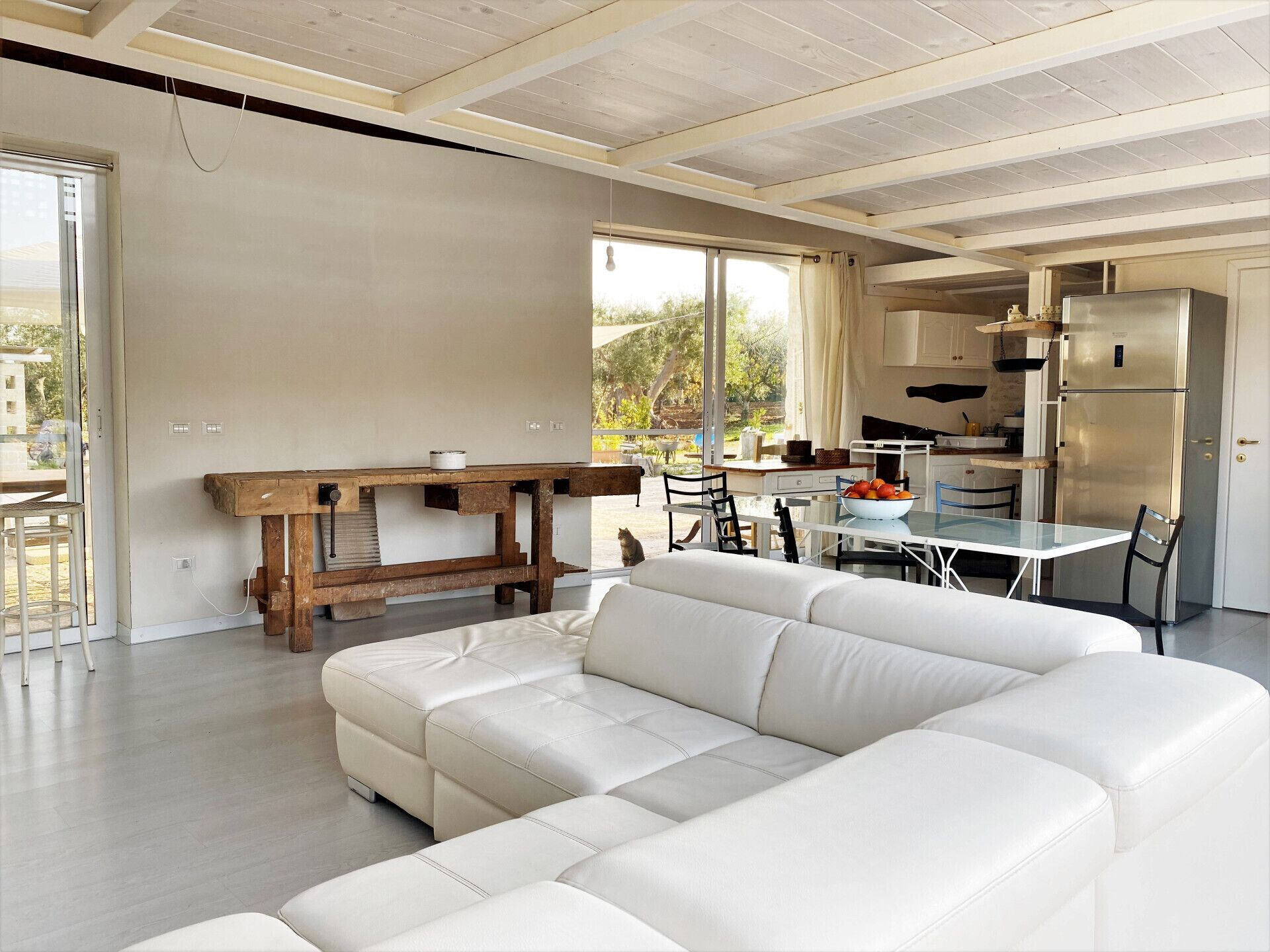 A modern living room with a white sofa, a wooden table, and a kitchen area with a refrigerator.