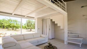 Un salon spacieux avec un canapé blanc, une petite table basse ronde agrémentée d’une plante, et un escalier menant à un niveau supérieur.