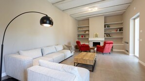 Een moderne woonkamer met een hoekbank, een salontafel en rode stoelen. Achtergrond met boekenkasten en een open haard.