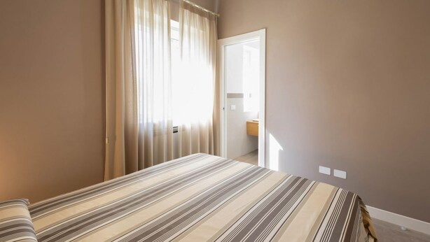 A bedroom with a bed, a window with curtains, and a door leading to a bathroom. - WePuglia - Dimora Montaltino (Castellana Grotte)