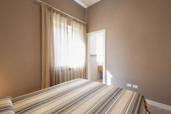 Ein Schlafzimmer mit einem Bett, einem Fenster mit Vorhängen und einer Tür zu einem Badezimmer.