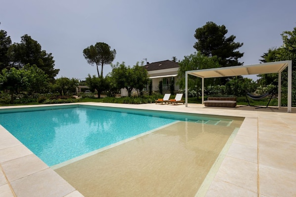Piscina com espreguiçadeiras e área de estar coberta.