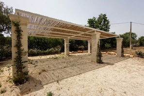 Ein überdachter Außenbereich mit Pergola, Betonpfeilern und einem Kiesplatz.