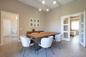 A modern dining area with a wooden table and white chairs, a small plant on the table, and framed pictures on the wall.