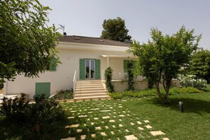 Uma casa térrea com entrada frontal, um pequeno alpendre e um jardim com um caminho de pedra até a porta.
