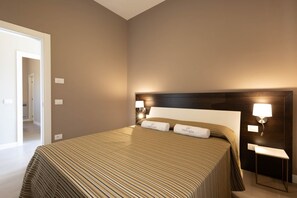 Ein Hotelzimmer mit einem großen Bett, einem Nachttisch mit Lampe und einer Tür zu einem weiteren Raum.
