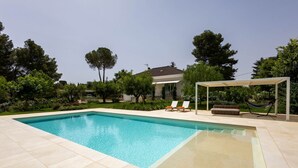 A rectangular swimming pool with a tiled deck, surrounded by greenery and a house in the background. - WePuglia - Dimora Montaltino (Castellana Grotte)