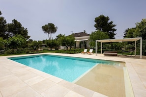 Ein rechteckiger Pool mit Fliesen umgeben von Grünflächen und einem Haus im Hintergrund.