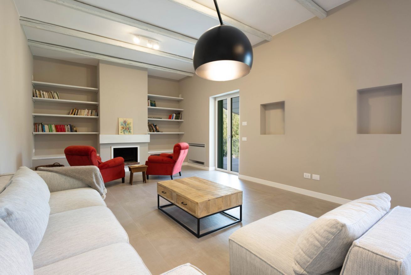 Een moderne woonkamer met een bank, rode stoelen, een salontafel en boekenkasten.